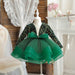 Green dress with sequin top and bow on a mannequin against a decorative background.