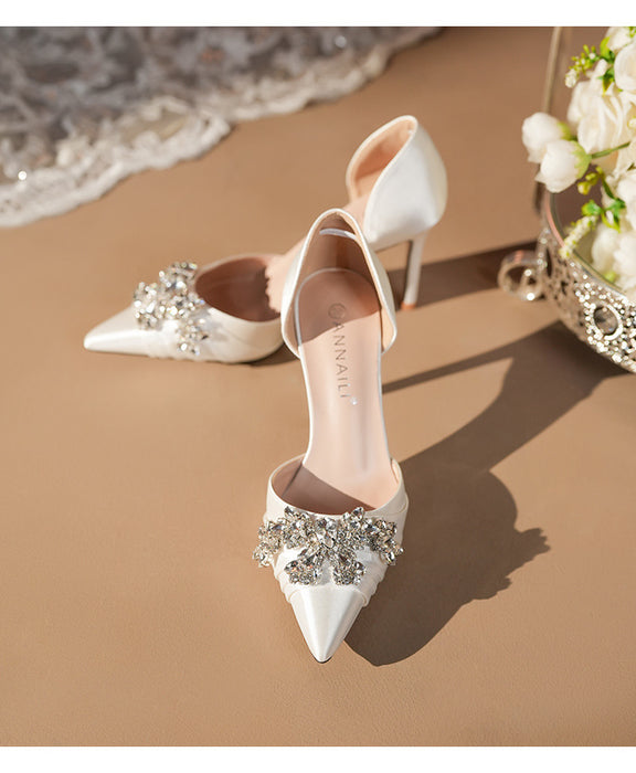 White high-heeled shoes with embellishments on a sandy surface with flowers.