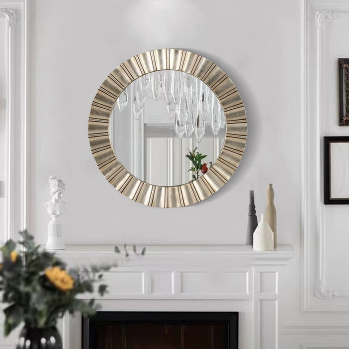 Round decorative mirror with a gold frame on a white wall above a fireplace.