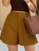Person wearing mustard yellow shorts and a brown top, holding a matching handbag.