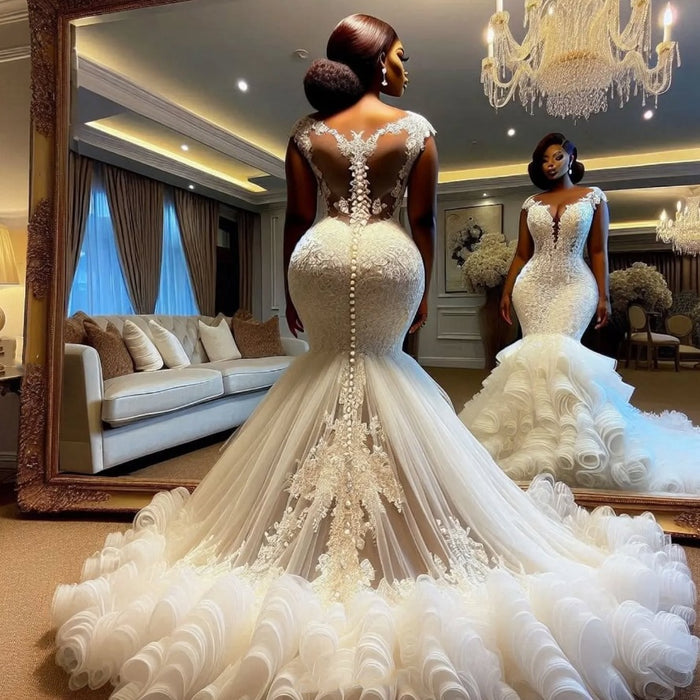 Woman in a white wedding dress standing in front of a large mirror in a luxurious room with chandeliers.