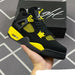 Black and yellow sneaker held by a hand with a black box featuring a logo in the background.