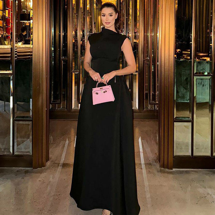 Woman in a black dress holding a pink handbag with a unique design, standing in an elegant interior setting.