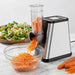 Vegetable chopper with carrots being shredded into a bowl on a marble countertop.