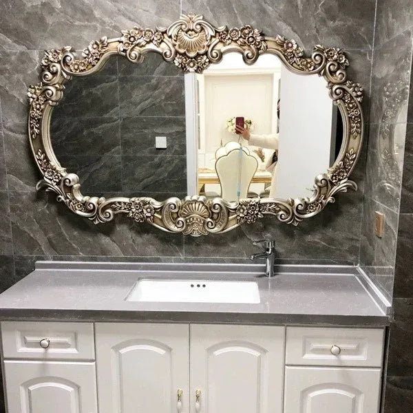 Decorative mirror with ornate frame above a sink in a bathroom setting.