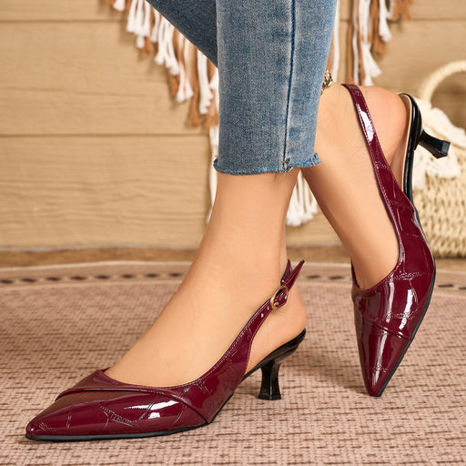 A pair of pointed-toe slingback pumps in glossy burgundy patent leather with kitten heels, shown on a model wearing blue jeans in a cozy indoor setting.