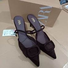 Black pointed-toe shoes with a bow detail on a light brown surface, with a Zara box in the background.