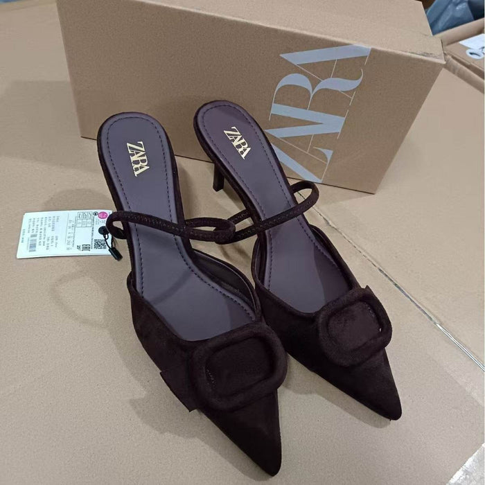 Black high-heeled shoes with a bow detail on a beige surface, with a Zara box in the background.
