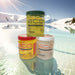 Three jars of Eco Styling Oil on a reflective surface with a snowy mountain landscape in the background