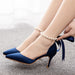 Blue high-heeled shoes with a bow and pearl anklets on a neutral background