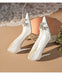 White high-heeled shoes with embellishments on a beige surface.