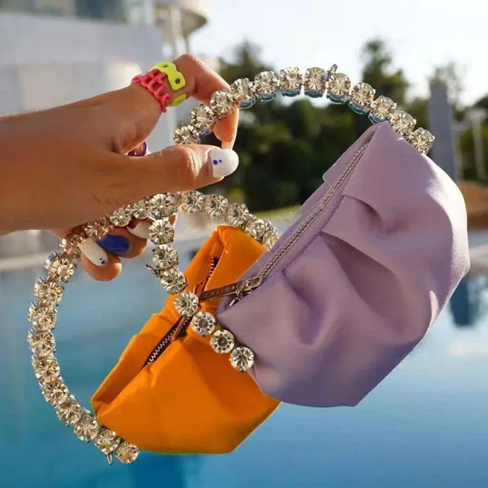 Hand holding a purple clutch with a decorative headband against a blurred outdoor background