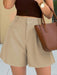 Person wearing beige shorts and a brown top, holding a brown handbag.