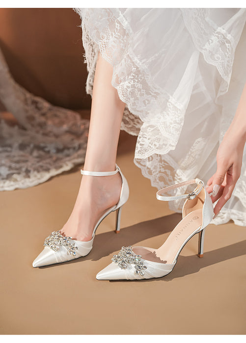White high-heeled shoes with embellishments worn by a person in a white lace dress.