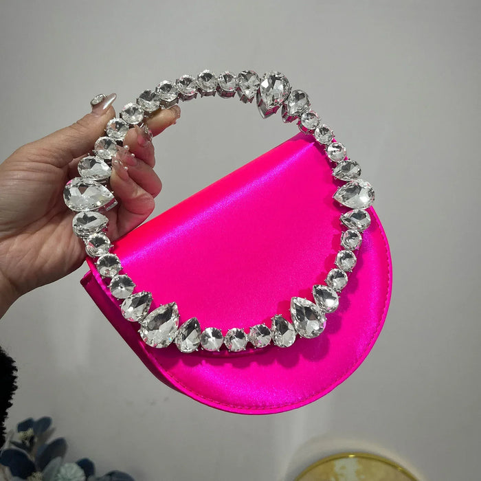 Pink handbag with a decorative crystal handle held by a hand against a neutral background