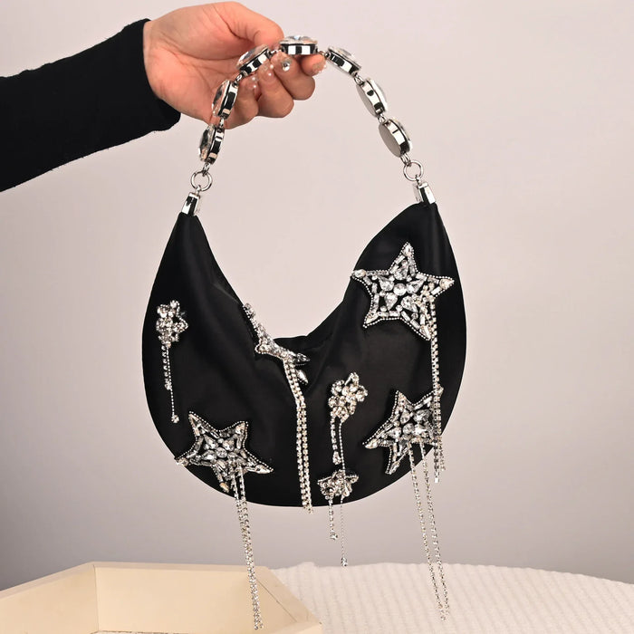 Black handbag with star designs and chains held by a hand against a neutral background