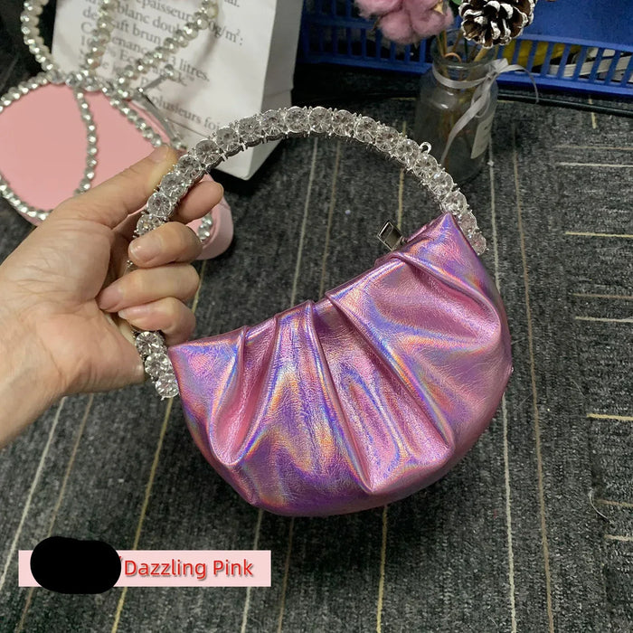 Hand holding a iridescent pink handbag with decorative handle on a textured surface.