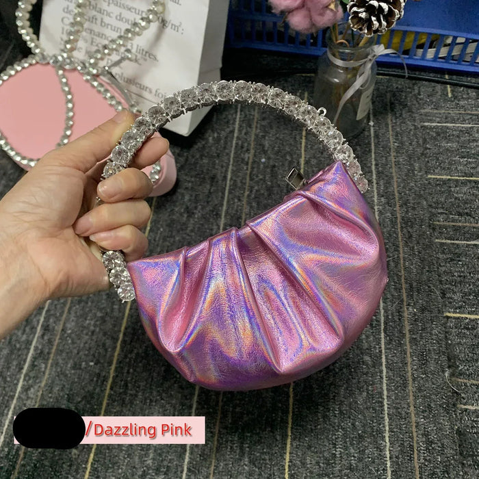 Hand holding a iridescent pink handbag with decorative handle on a textured surface.