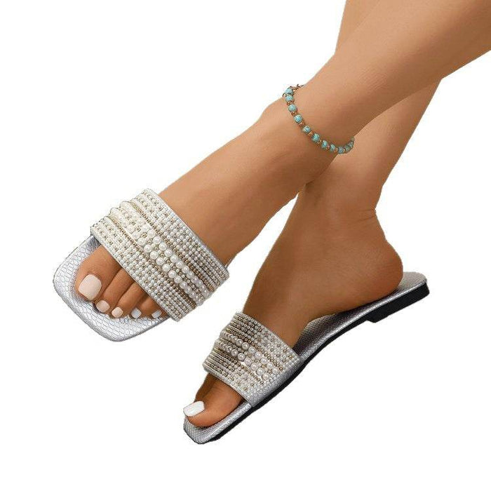 Silver embellished sandals worn on feet with a white background
