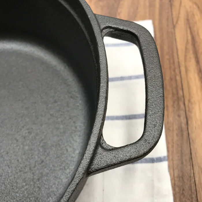 Close-up of a cast iron skillet handle on a wooden surface with a striped cloth underneath.