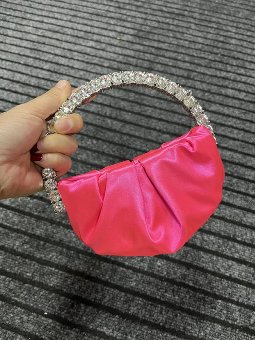 Pink handbag with a decorative handle held by a hand on a textured gray background