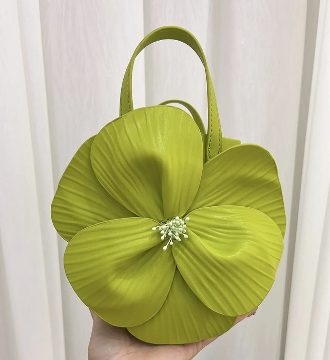 Green floral handbag held against a white curtain background
