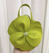Green floral handbag held against a white curtain background