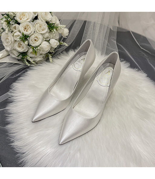 Silver high-heeled shoes on a white fur surface with a bouquet of white roses.