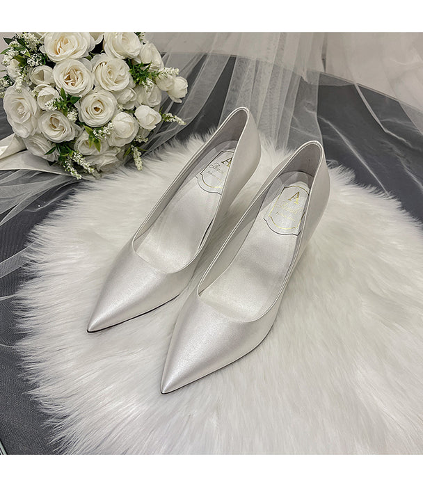 Silver high-heeled shoes on a white fur surface with a bouquet of white roses.