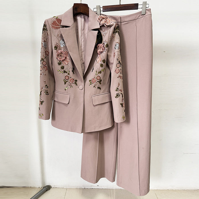 Pink suit with floral embroidery on a hanger against a white wall.