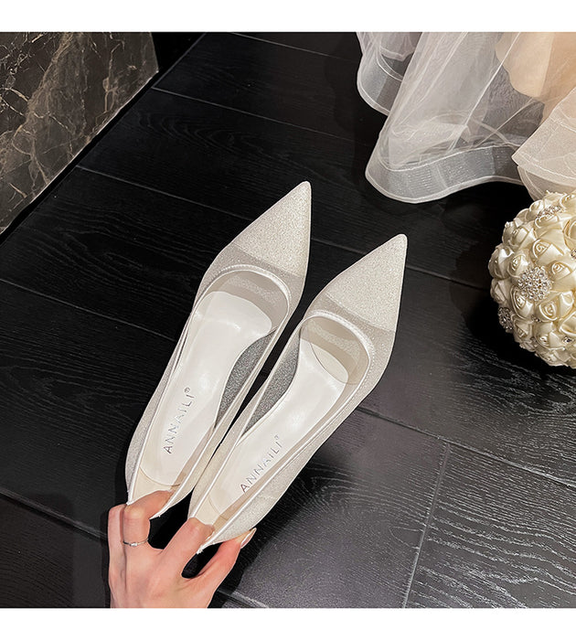 Pair of white pointed-toe shoes held by a hand on a dark wooden floor.