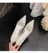 Pair of white pointed-toe shoes held by a hand on a dark wooden floor.