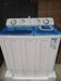 White and blue washing machine on a tiled floor with a cardboard box in the background