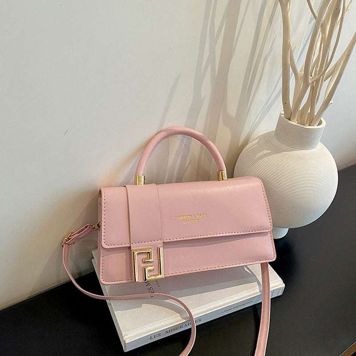 A pink faux leather handbag with a gold FF logo clasp, resting on a white book next to a white vase with dried branches.