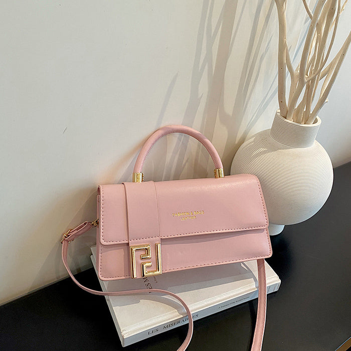 A pink faux leather handbag with a gold FF logo clasp, resting on a white book next to a white vase with dried branches.