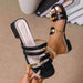 Black strappy sandals with gold accents worn by a person on a beige surface.
