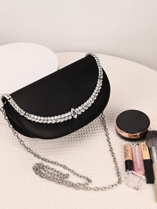 Black handbag with silver chain and embellishments on a white surface with makeup items.