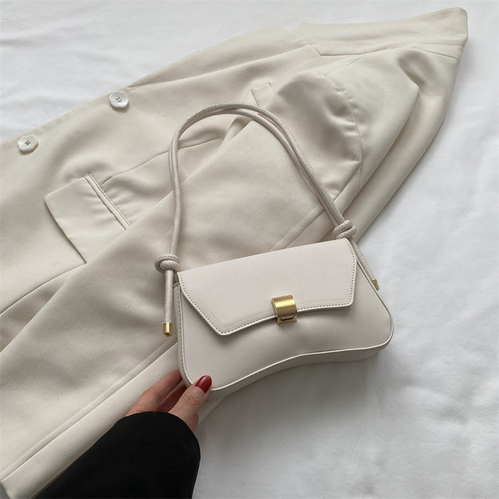 White handbag with gold accent held by a hand against a white coat on a white background