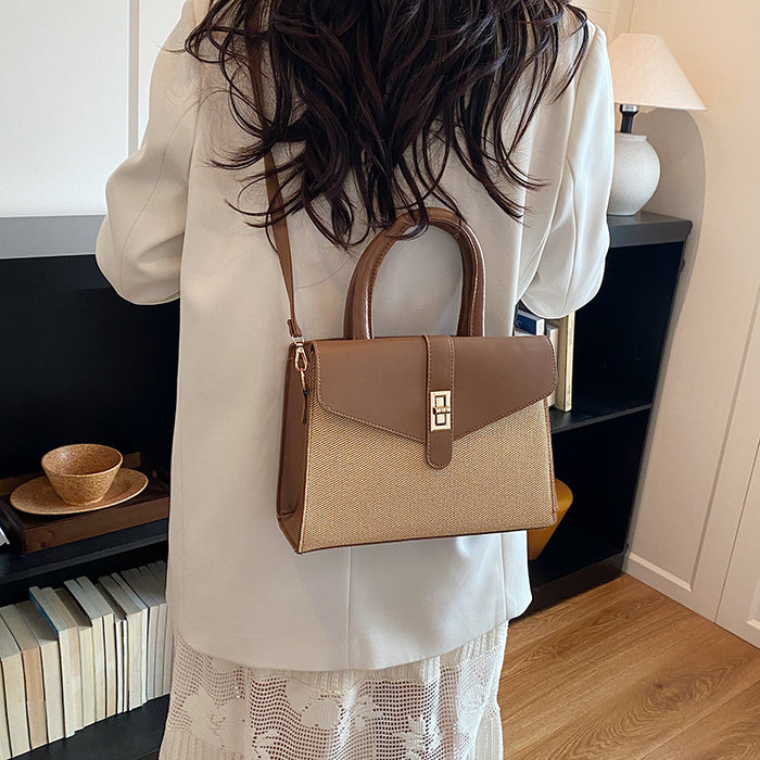 A woman viewed from behind wearing a structured handbag with a brown and beige color-blocked design, featuring a top handle, a shoulder strap, and a gold-tone turn-lock clasp, set against an indoor home background.