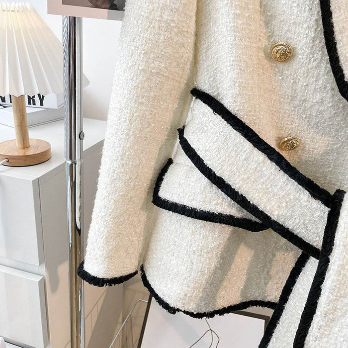 White textured jacket with black trim and gold buttons in a minimal indoor setting.