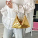 A person wearing a white ruffled blouse and light gray pants carries a small triangular gold sequin shoulder bag with a thin gold strap.