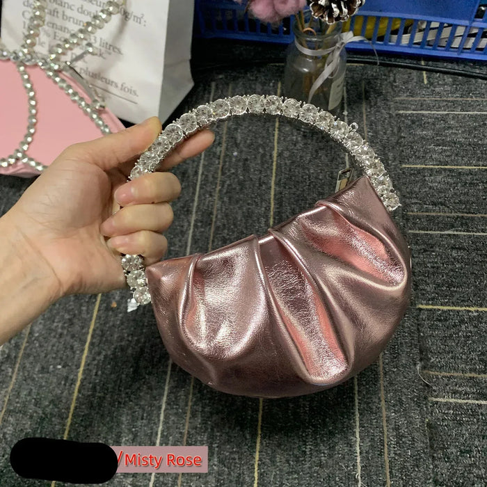 Rose gold handbag with decorative handle held by a hand on a textured surface.