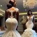 Woman in a white lace wedding dress standing in a room with a chandelier.