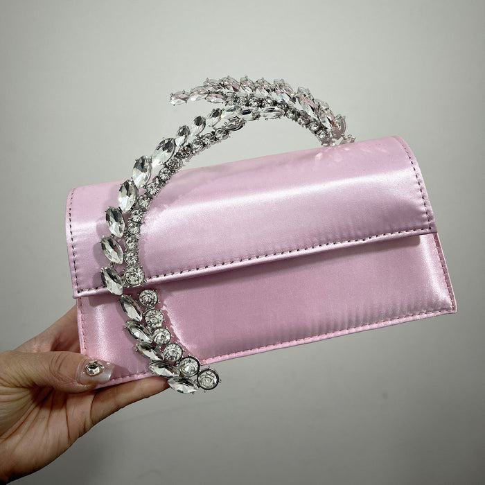 Pink handbag with decorative handle held by a hand against a gray background