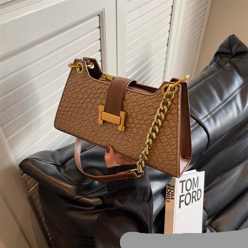 Brown handbag with gold chain on a black surface, with a Tom Ford card in the foreground.