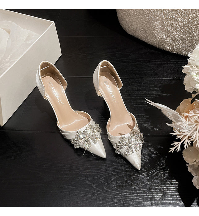 Pair of silver high-heeled shoes with embellishments on a dark wooden surface.
