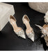 Pair of silver high-heeled shoes with embellishments on a dark wooden surface.