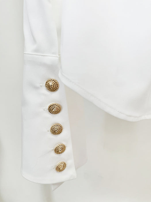 Close-up of a white garment with gold buttons on a light background