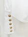 Close-up of a white garment with gold buttons on a light background
