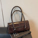 A dark brown leather handbag with double top handles and a flap closure, displayed on top of a black book against a light beige textured wall.
